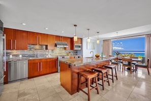 A modern kitchen with wooden cabinets, stainless steel appliances, and a large island with bar stools. - 2 Honua Kai Villas | Ocean Front | Sleeps 16 | Free Car w/ 6+ Nights | ML-3191 (Lahaina)