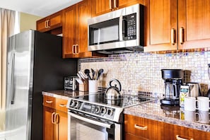 A modern kitchen with stainless steel appliances, wooden cabinets, a tiled backsplash, and a coffee maker. - 2 Honua Kai Villas | Ocean Front | Sleeps 14 | Free Car w/ 6+ Nights | ML-3197 (Lahaina)