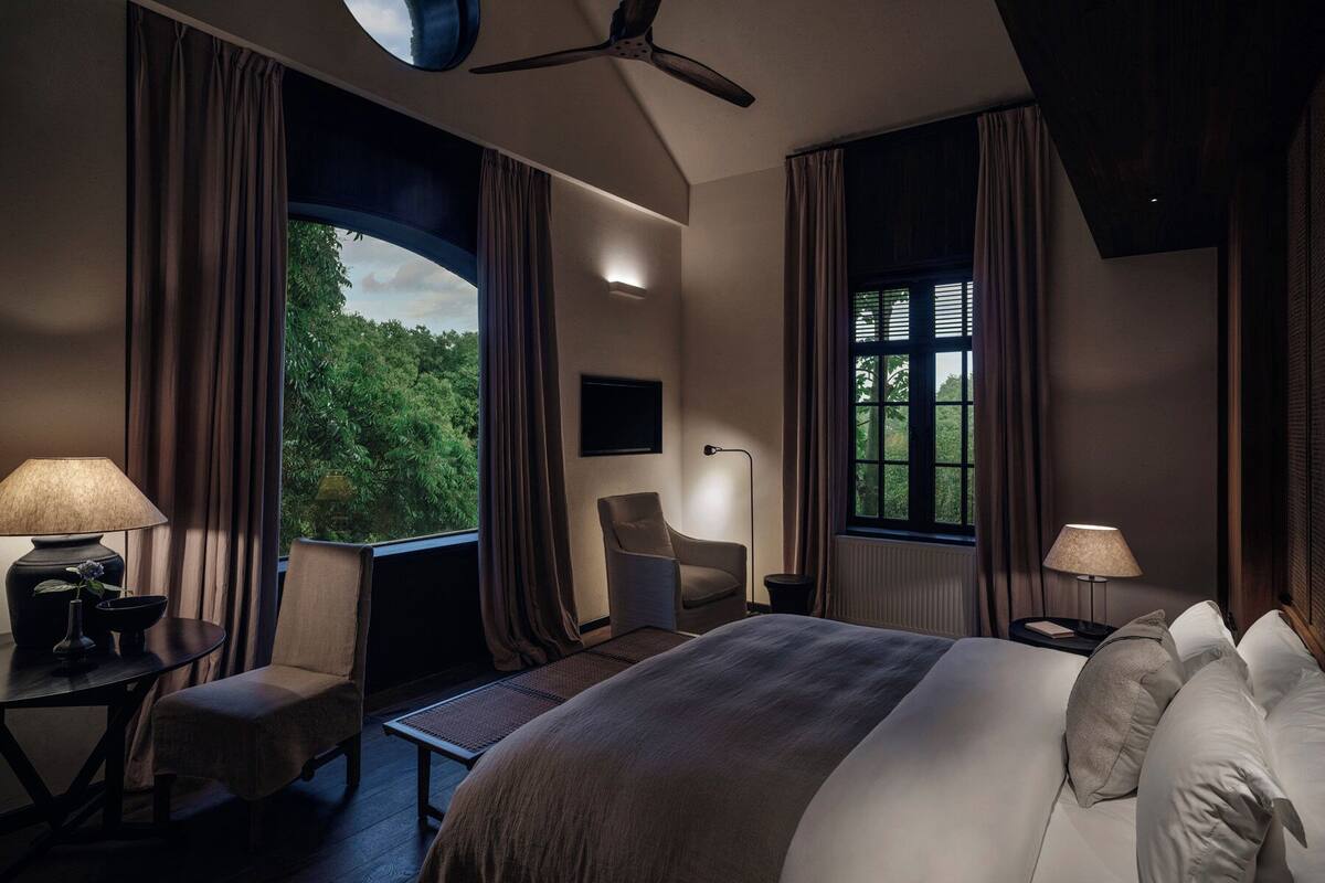 A bedroom with a bed, a chair, a desk, a window with curtains, and a ceiling fan.