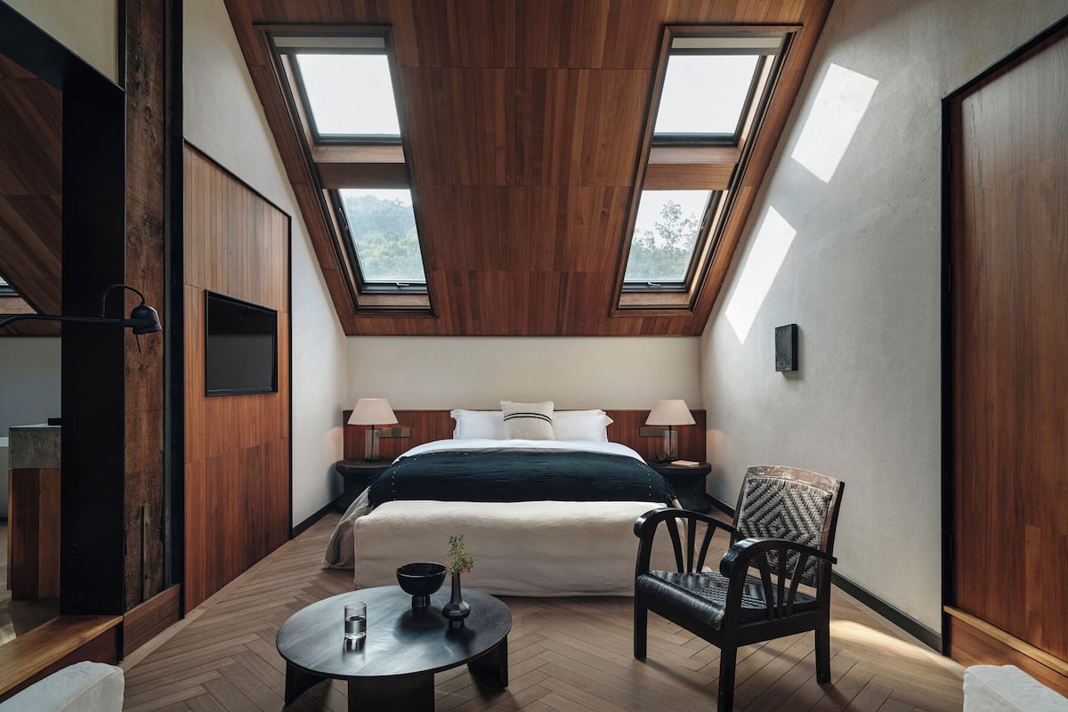 A room with a bed, two bedside tables, a chair, a round table, and skylights.