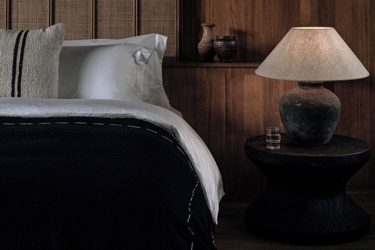 A bedroom with a bed, pillows, a bedside table with a lamp, and a wall with vertical wooden panels.