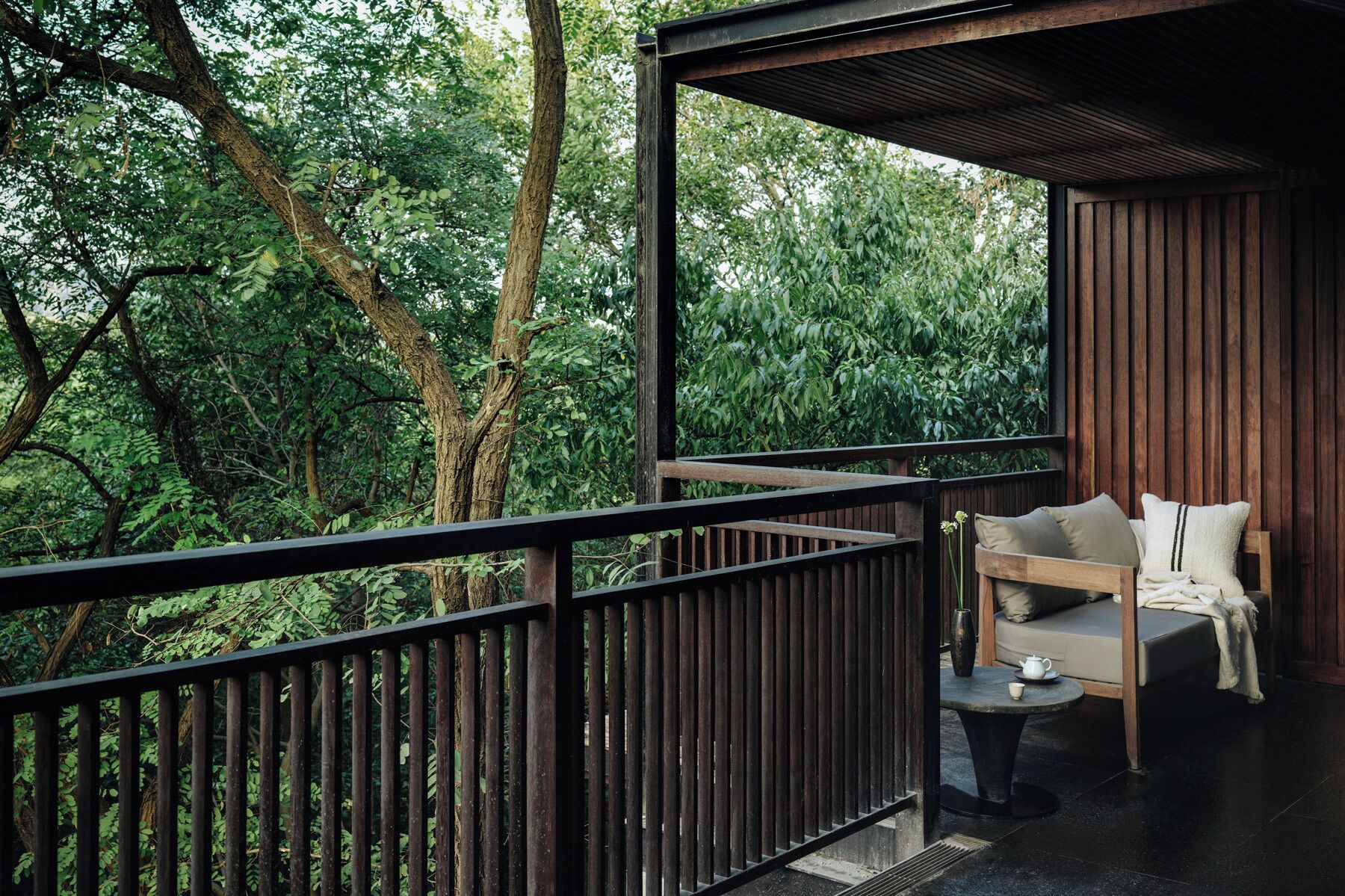 Un balcon avec une balustrade en bois, un canapé avec des coussins et une petite table sur laquelle se trouvent une tasse et une soucoupe.