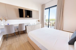 A hotel room with a bed, a desk with chairs, a flat-screen TV, and a balcony with outdoor seating. - Luxury Suite Downtown Punta Cana. 2 min Walk to Coco Bongo • Pool, Gym & Parking (Punta Cana)