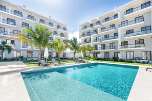 A modern hotel with a swimming pool, multiple balconies, and palm trees. - Luxury Suite Downtown Punta Cana. 2 min Walk to Coco Bongo • Pool, Gym & Parking (Punta Cana)