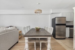 A dining area with a wooden table, white chairs, a chandelier, a sofa, and a modern kitchen with a stainless steel refrigerator. - 2-story Condo with Private Balcony, Ocean Views and Community Pool (Isle Of Palms)