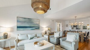 Een woonkamer met een bank, fauteuils, een salontafel en een eethoek met een kroonluchter.