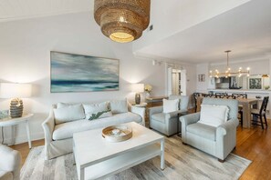A living room with a sofa, armchairs, a coffee table, and a dining area with a chandelier. - Steps to Beach + Pool Access (Isle Of Palms)