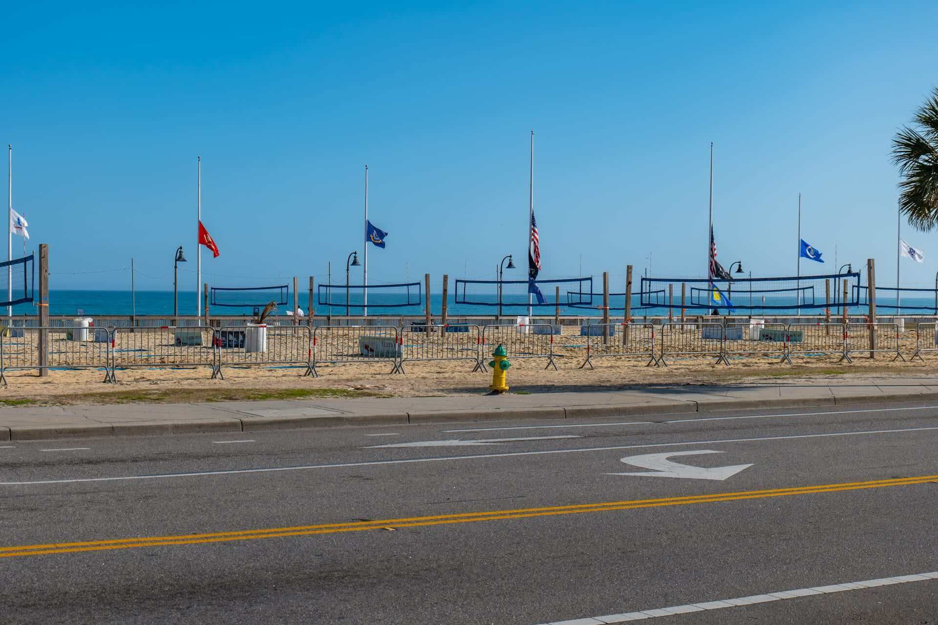 A beach with a volleyball net, a yellow fire hydrant, and multiple flags.