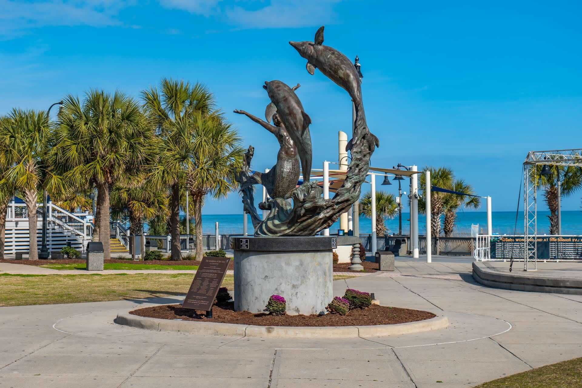 A sculpture of dolphins in a public park with a clear view of the ocean in the background.