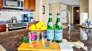 Eine Küche mit Mikrowelle, Herd und einer Schüssel Zitronen. Auf einem Schneidebrett stehen zwei Pellegrino-Flaschen und zwei Gläser.