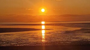 A sunset over a beach with calm water reflecting the sun.