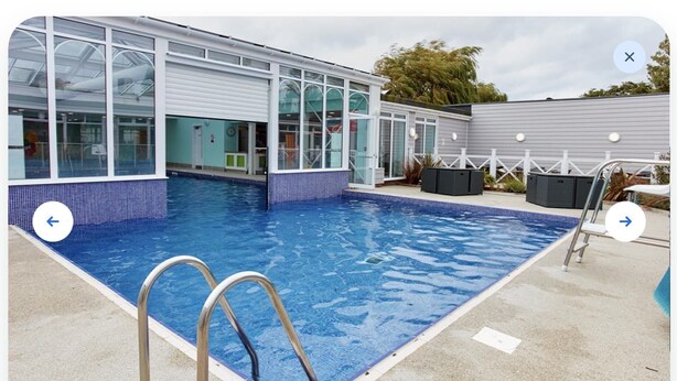 A swimming pool with a glass enclosure, a metal ladder, and a fenced area with outdoor seating.