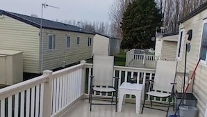A covered outdoor area with a white railing, two chairs, a small table, and a broom leaning against the railing.