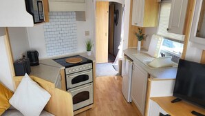 Een compacte camperkeuken met een kookplaat, oven, gootsteen en een kleine televisie.