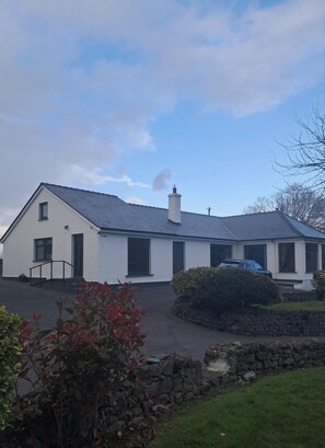 A white building with a grey roof, a stone wall, and a driveway. - Apartment - Sleeps 3 - Westport , Free Parking (WESTPORT, CO MAYO)