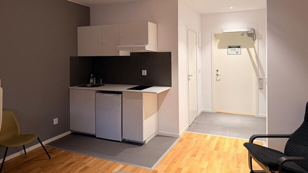 Een compacte keuken met moderne apparatuur, een klein eethoekje en een deur naar een gang.