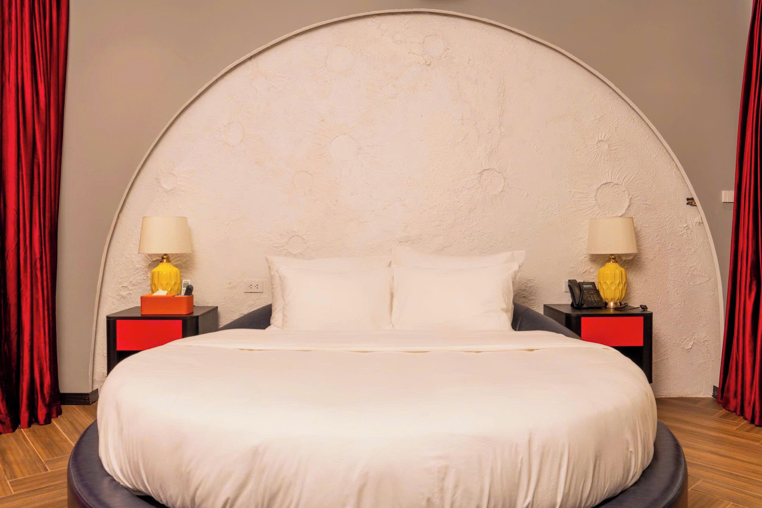 A bed with white linens, two bedside tables with lamps, and red curtains.
