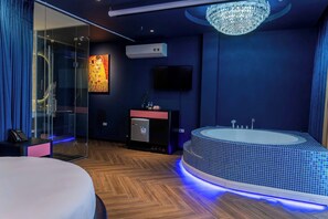 A modern hotel room with a glass shower enclosure, a large bathtub with blue-tiled surround, a flat-screen TV, and a chandelier. - Min Hotel Ha Noi (Yen Hoa)