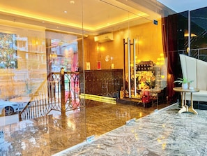 Un moderno vestíbulo de hotel con piso de mármol, una escalera y un área de descanso con una mesa pequeña y sillas.