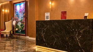 Zona de recepción de un hotel con un mostrador de mármol, una silla, un cuadro decorativo y un cartel con código QR.