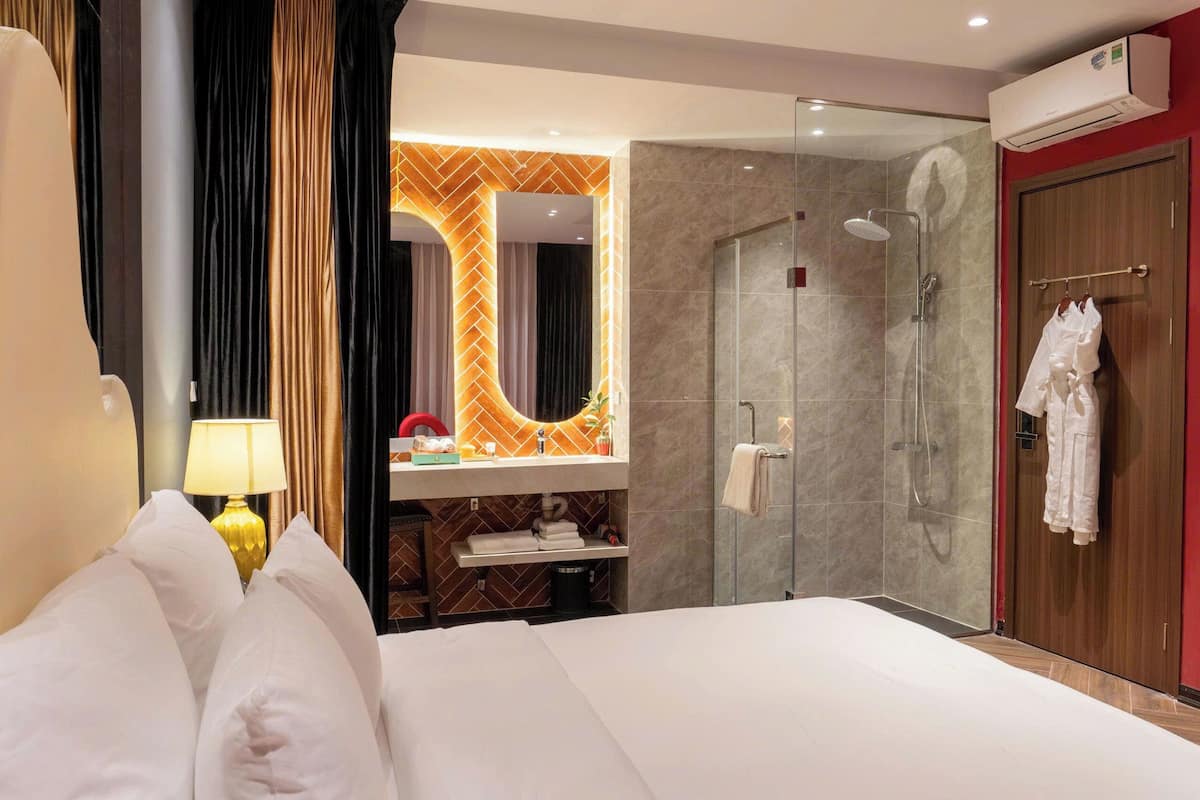 A hotel room with a bed, a bathroom with a shower, a vanity, and a mirror.