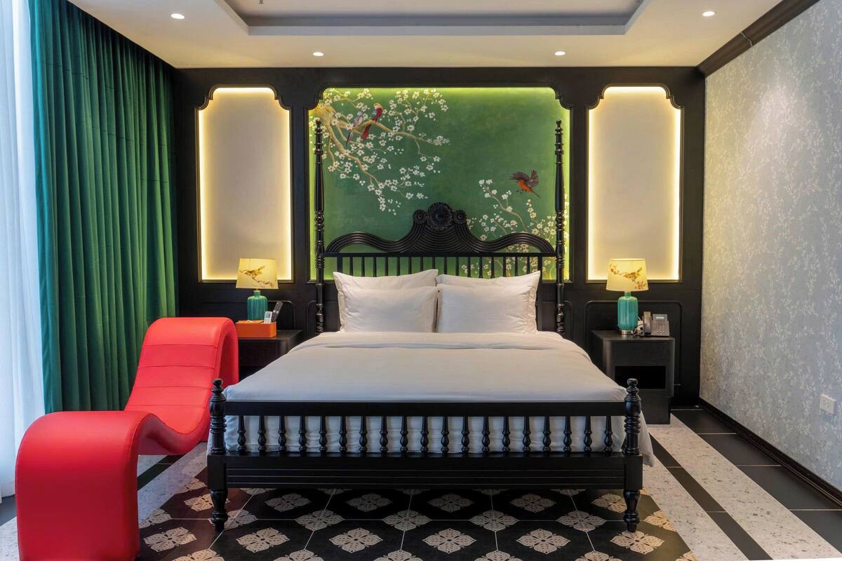 A bedroom with a bed, nightstands, a red chair, and a green wall with a floral mural.