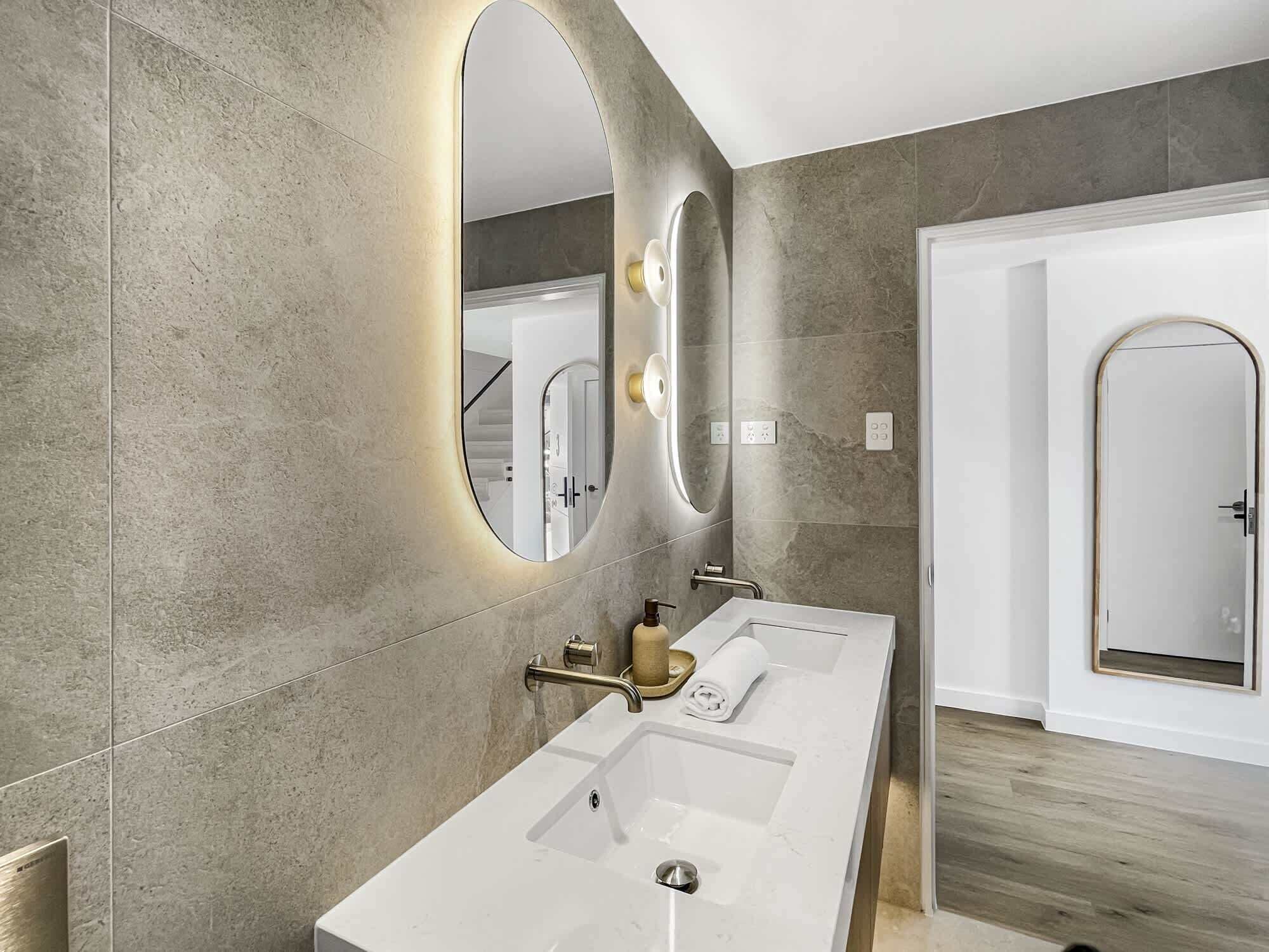 Une salle de bain moderne avec un double vasque, un grand miroir et un porte-serviettes.