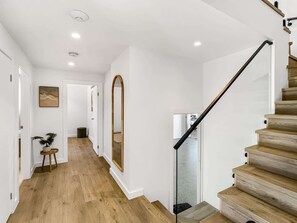 A modern interior with a wooden staircase, white walls, and a hallway leading to a door.