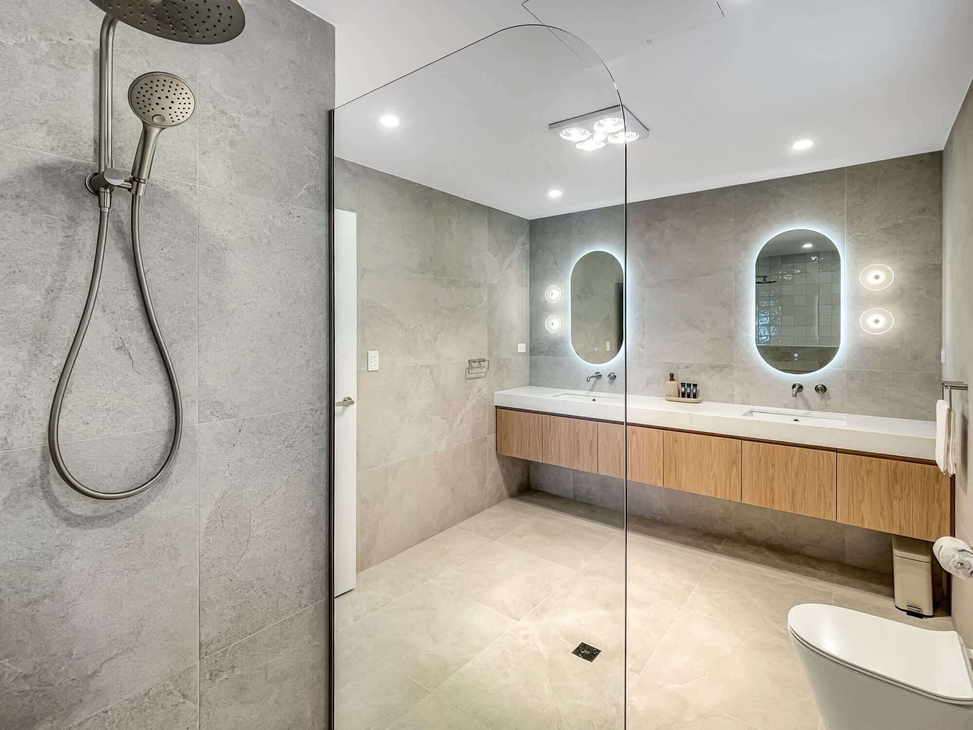 A modern bathroom with a shower, two mirrors, a sink, and a toilet.