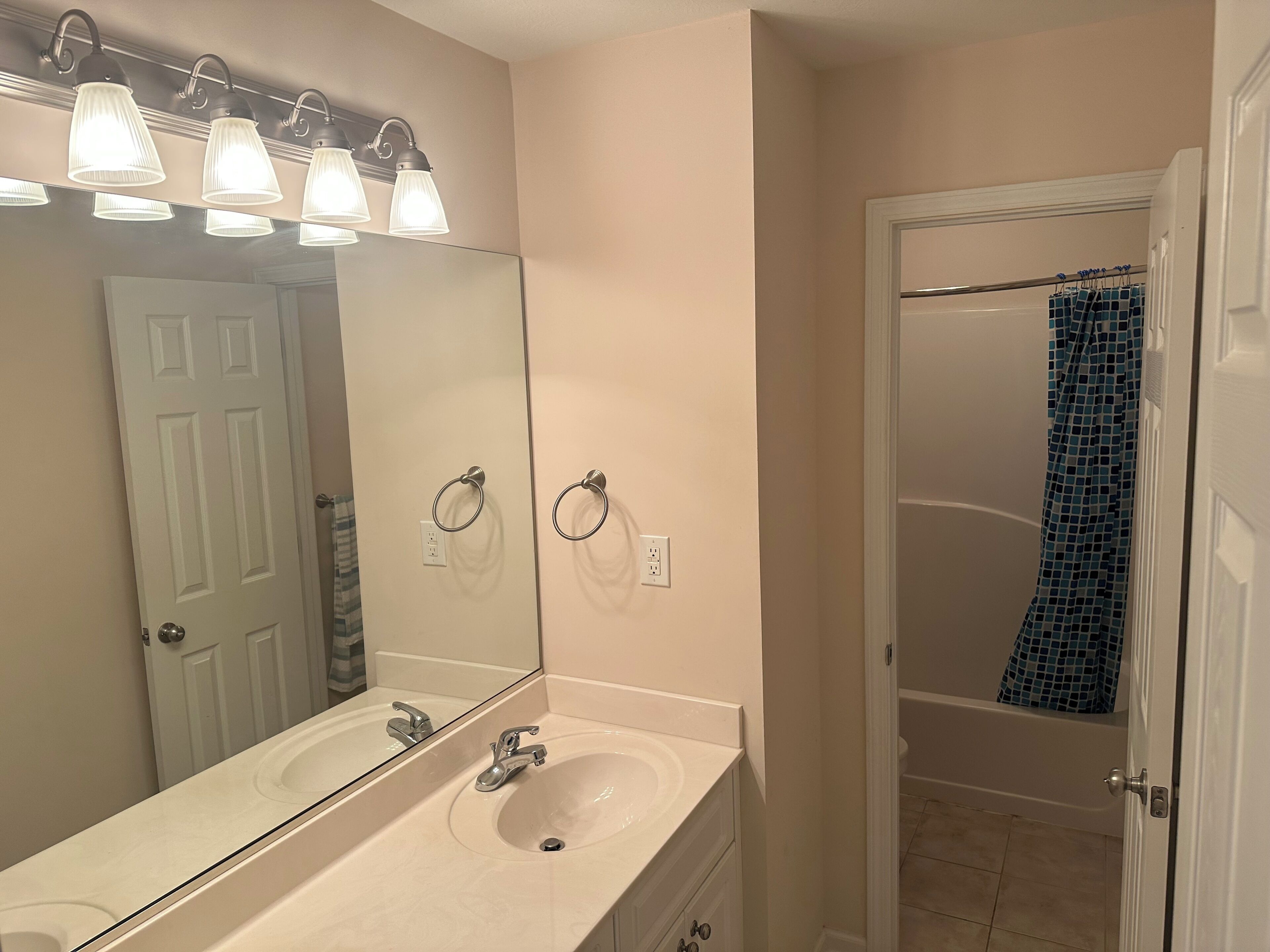 A bathroom with a double sink, a large mirror, and a shower curtain.