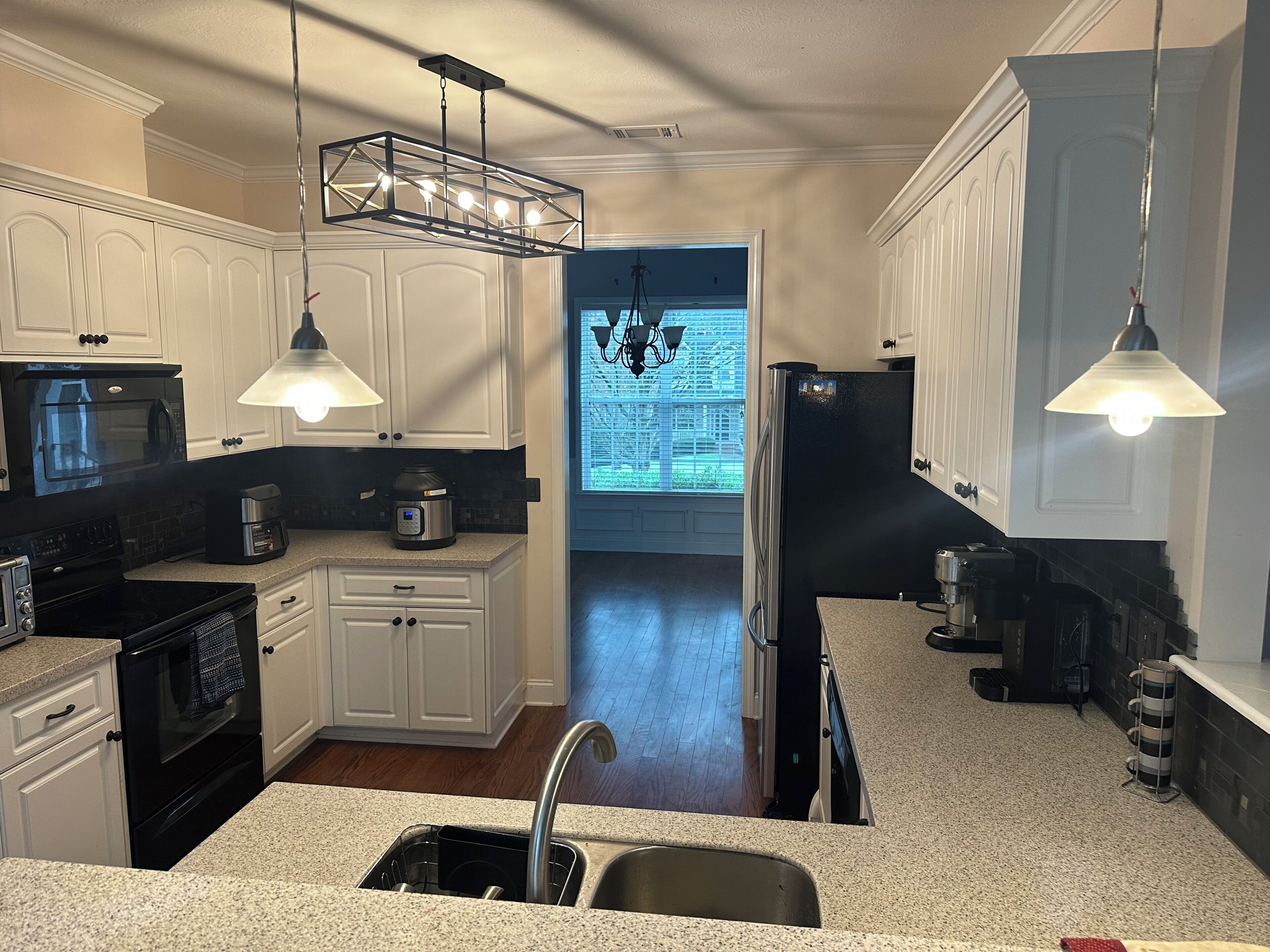 A kitchen with white cabinets, a black refrigerator, a microwave, a stove, and a sink.