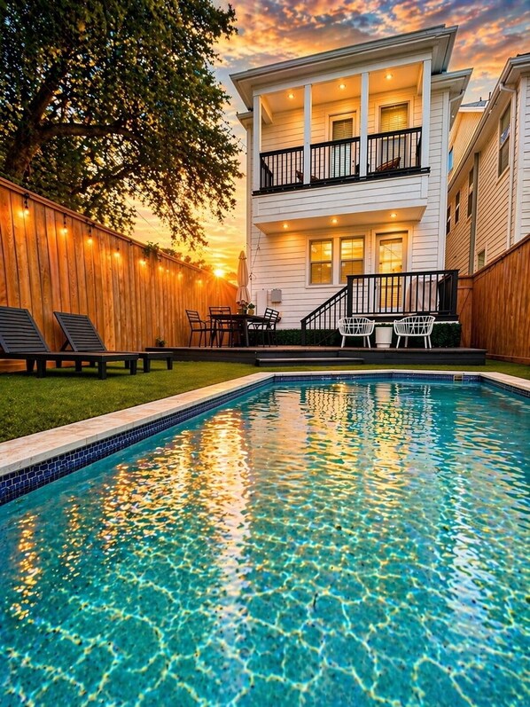 Una casa de dos pisos con piscina, mobiliario exterior y valla de madera.
