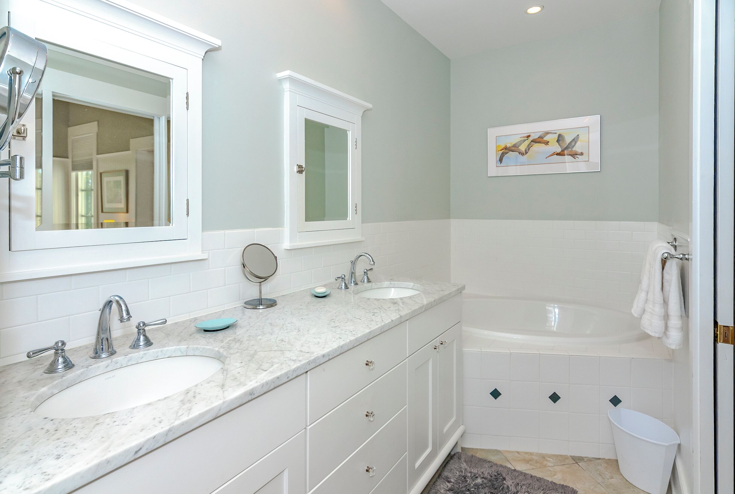 Une salle de bain avec deux lavabos, un grand miroir, un tableau encadré et une baignoire.