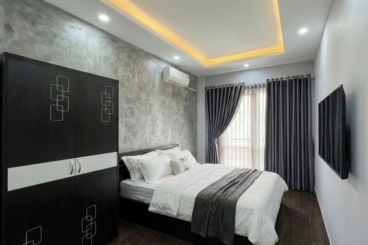 A modern bedroom with a bed, a wardrobe, an air conditioning unit, and a TV mounted on the wall.