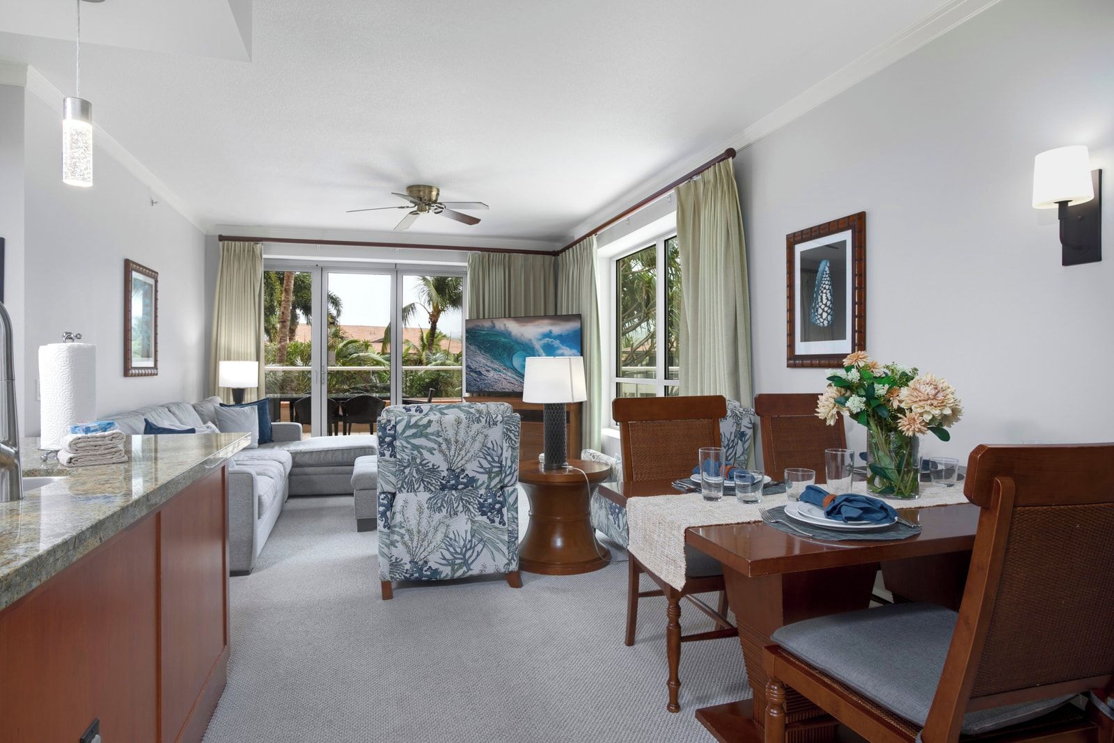Habitación de hotel con zona de comedor, sofá, sillón, mesa para dos personas y ventilador de techo.