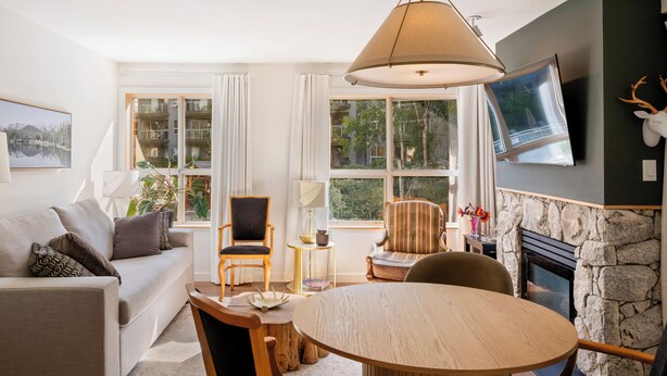 Una sala de estar con sofá, sillas, mesa, chimenea y televisor montado en la pared.