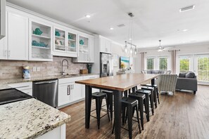 A modern kitchen with white cabinets, a wooden island with bar stools, stainless steel appliances, and a view to a living area with a gray sofa. - ⛱️Heated Community Pool-Gorgeous 4BR Townhome-Walk to beach-Emerald Escape⛱️ (Miramar Beach)