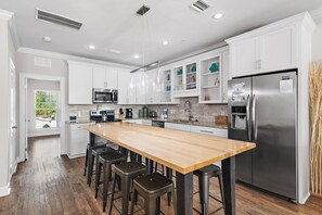 A modern kitchen with white cabinets, a stainless steel refrigerator, a wooden island with bar stools, and a view of the outdoors. - ⛱️Heated Community Pool-Gorgeous 4BR Townhome-Walk to beach-Emerald Escape⛱️ (Miramar Beach)