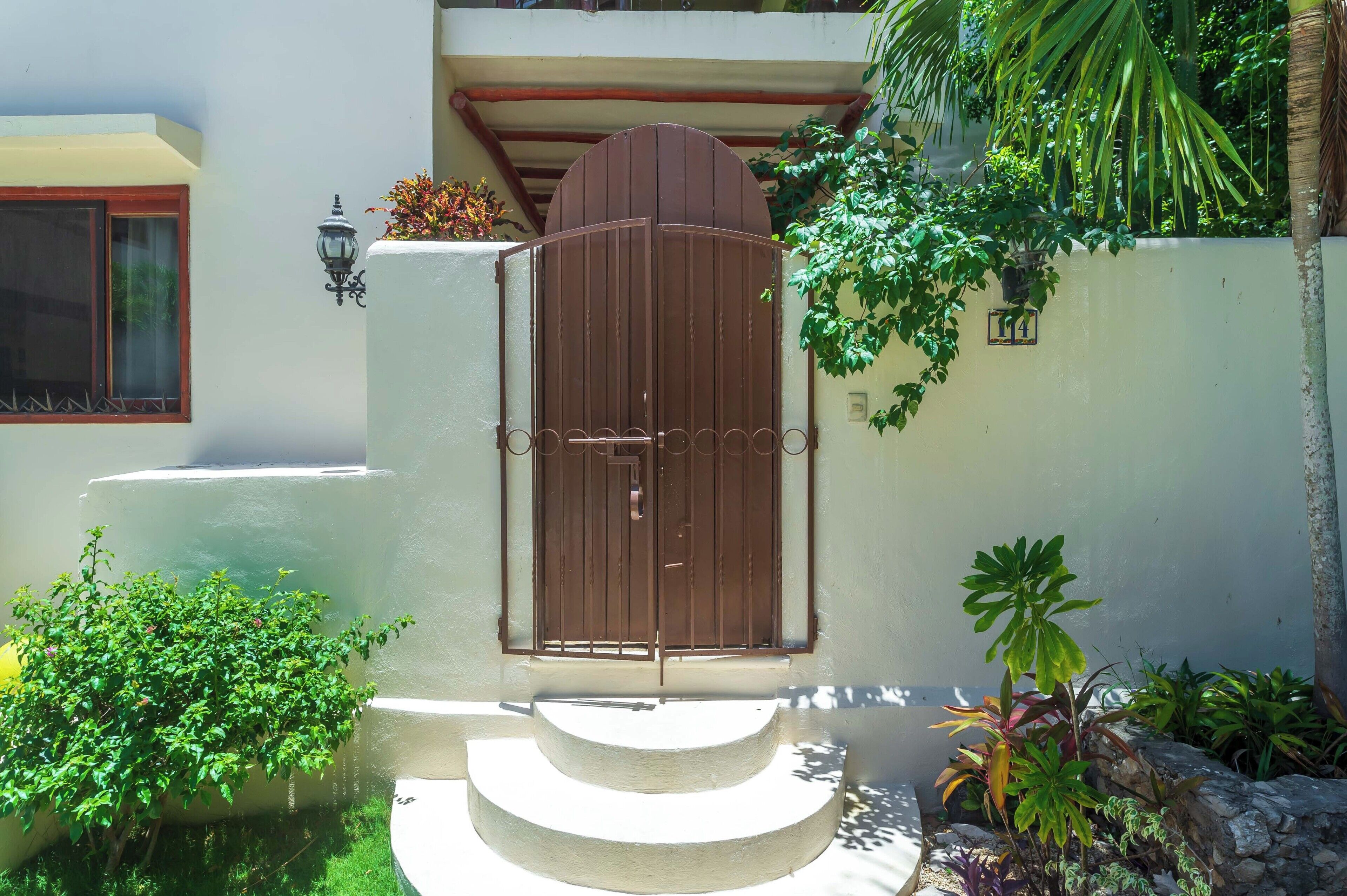 A gated entrance with a metal gate, a small staircase, and a wall-mounted light fixture.