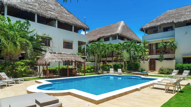 Ein Resort mit Pool, Liegestühlen und Gebäuden mit Reetdächern.