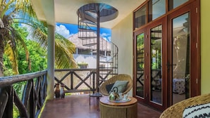 Ein Balkon mit Wendeltreppe, Korbmöbeln und Blick auf ein Haus mit Strohdach.