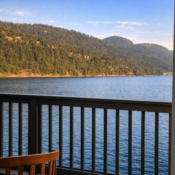 Vista de uma varanda com vista para um lago, com colinas arborizadas ao fundo.