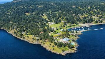 Vue aérienne d’une propriété située sur la côte, comprenant un port de plaisance, une zone forestière dense et des immeubles résidentiels.