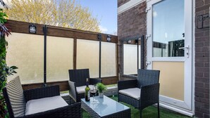 Une terrasse dotée de meubles en osier, d’une table en verre et d’une porte avec une fenêtre.
