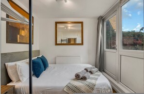 Ein Schlafzimmer mit Bett, Fenster, Heizkörper und Spiegel.