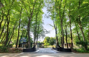 A residential area with a welcoming sign, a paved entrance, and tall trees.
