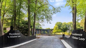Une entrée fermée par un portail donne accès à un quartier résidentiel appelé « ’t Kleine Loo », et une allée pavée mène à un bâtiment moderne.