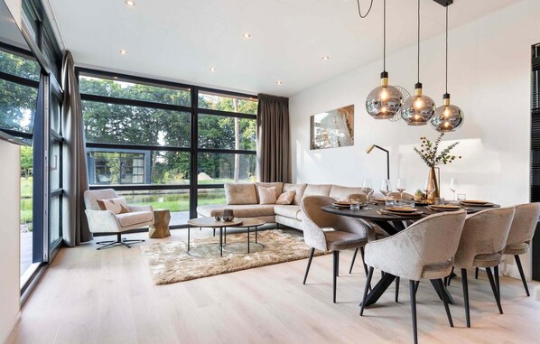 A modern living room with a large window, a dining area with a round table, and a sofa.