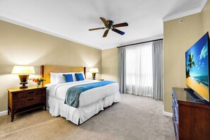 Ein Hotelzimmer mit Bett, Nachttischen, Lampen, Deckenventilator, Fernseher und einem großen Fenster mit Vorhängen.