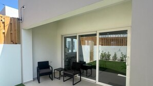 Eine moderne Terrasse mit Rasen, einer Sitzecke mit Stühlen und einem Tisch, und eine Glastür, die in einen Garten führt.